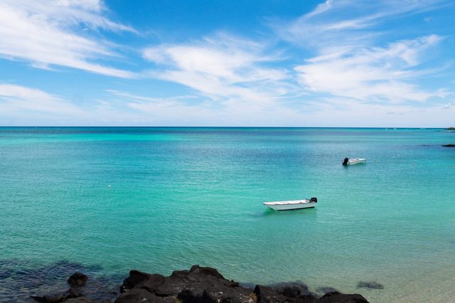 Two small boats float on turquoise ocean water under a clear blue sky, with black rocks in the foreground.