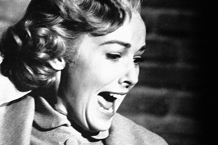 A person screams in fear, mouth open wide, with brick wall visible in the background, evoking an intense emotional reaction.