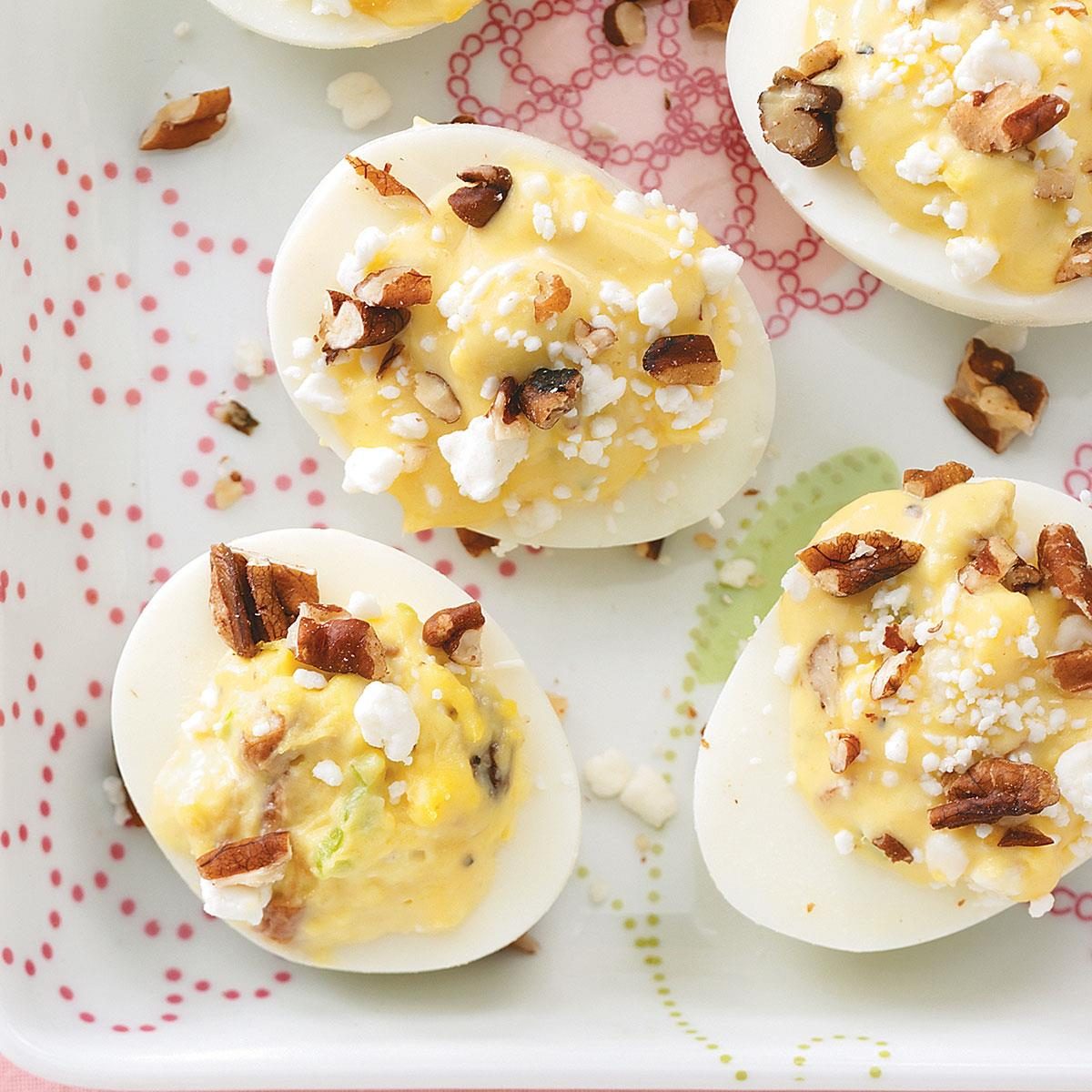 Deviled eggs topped with crumbled feta and pecans rest on a decorative, colorful-patterned plate.