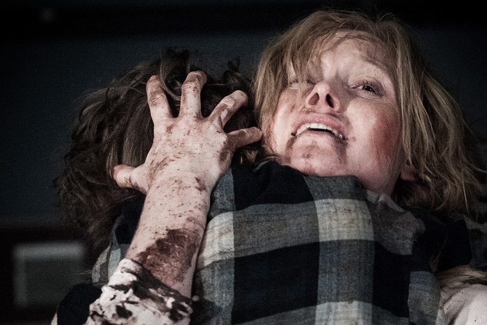 Two people embrace tightly, one with a dirt-smudged face and hand, in a dimly lit, tense atmosphere.