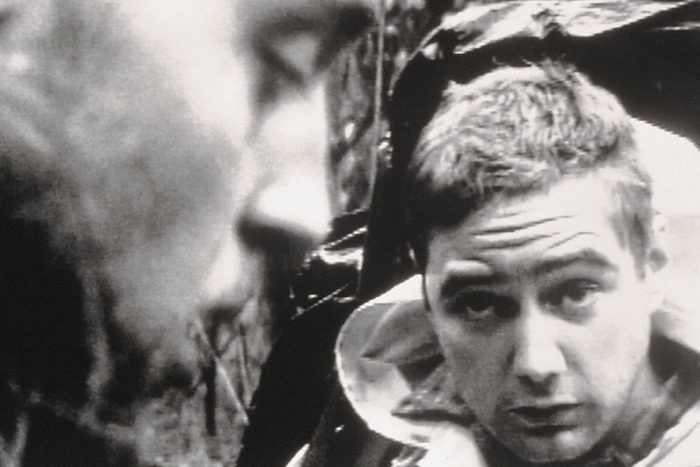 Two men, one focused and one blurred, in a black-and-white setting, creating an intense, introspective atmosphere.