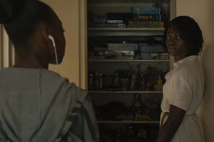 Person faces a woman wearing earphones, standing near a filled shelf in a dimly lit room.