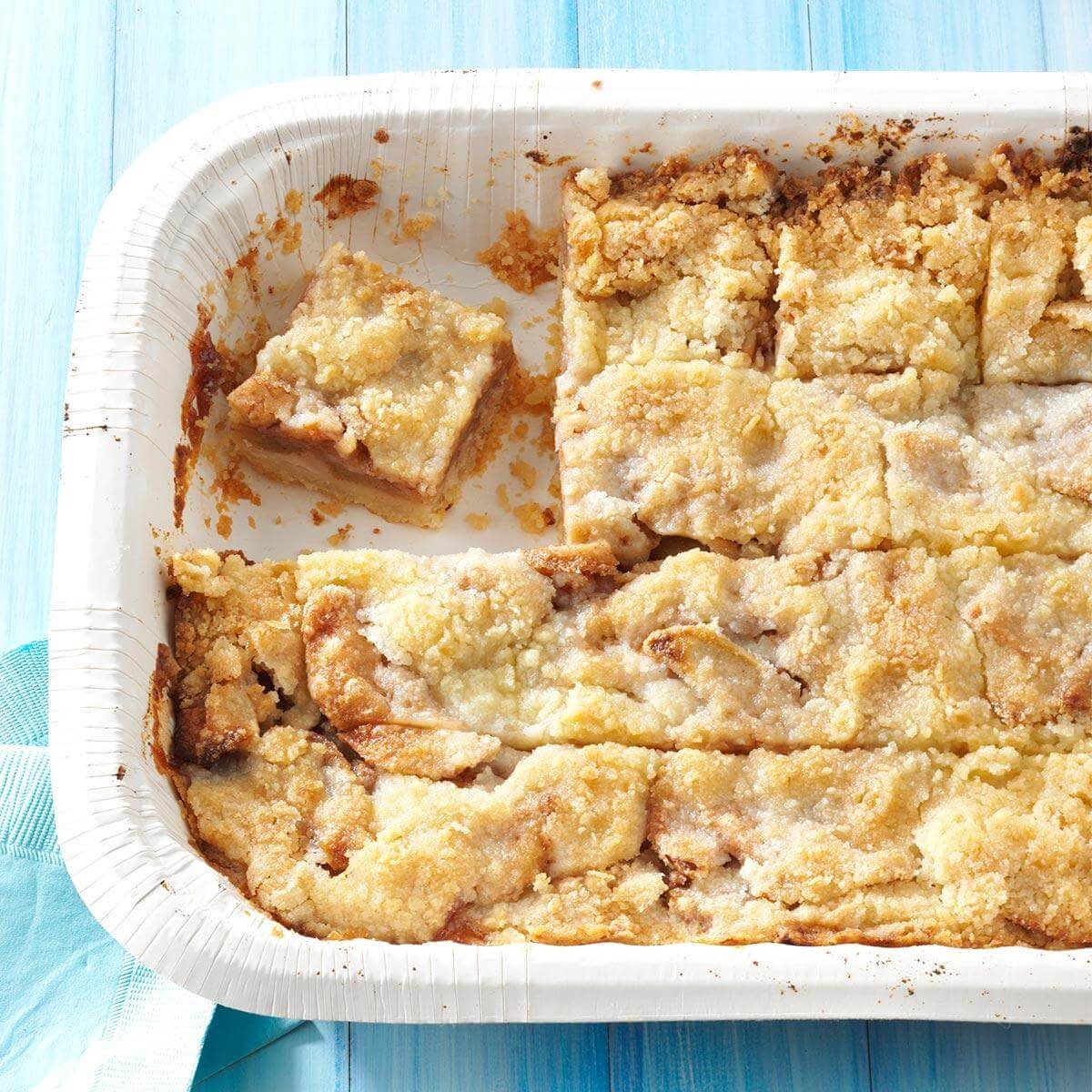 A partially eaten tray of crumb-covered bars rests on a light blue wooden surface, with one distinct square piece removed.
