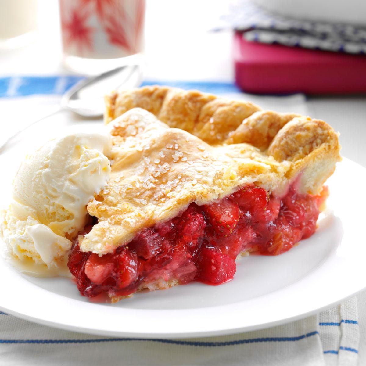 A slice of berry pie sits on a white plate, accompanied by a scoop of vanilla ice cream, on a table with a striped cloth.