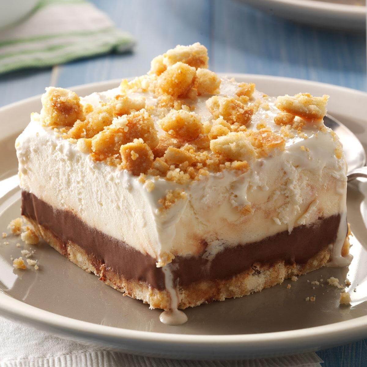 A layered ice cream dessert with chocolate and vanilla sections, topped with crumbled cookies, sits on a beige plate in a light, casual setting.