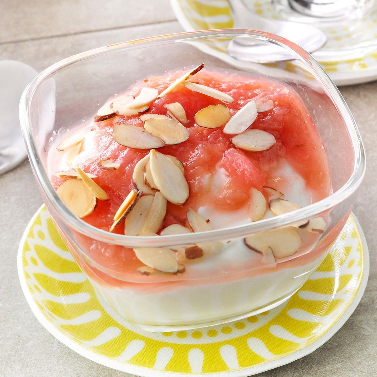 Yogurt topped with pink fruit compote and sliced almonds sits in a clear dish on a yellow-patterned plate.