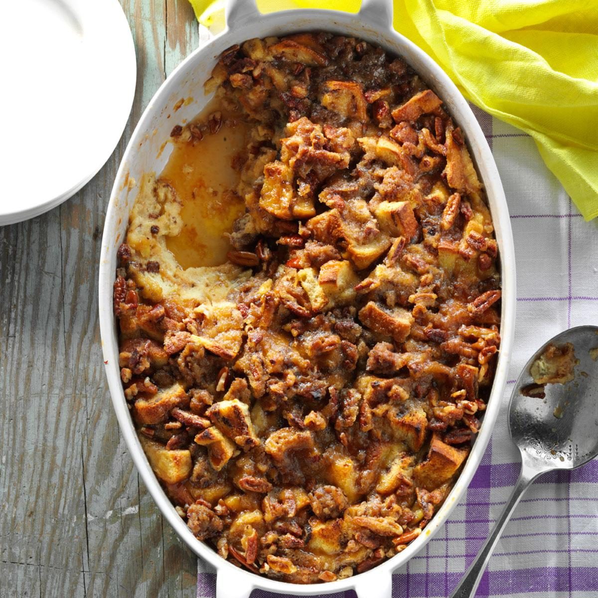 Casserole dish holding baked pecan dessert; one serving removed. Resting on rustic wooden table with a purple-striped cloth and scattered yellow fabric nearby.