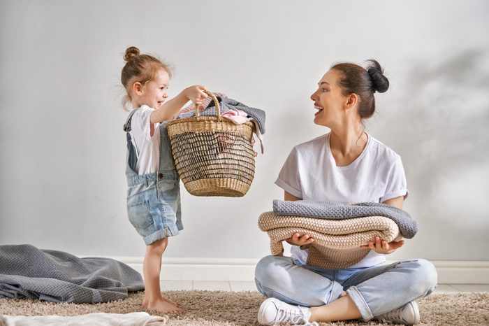 Beautiful young woman and child girl little helper are having fun and smiling while doing laundry at home.