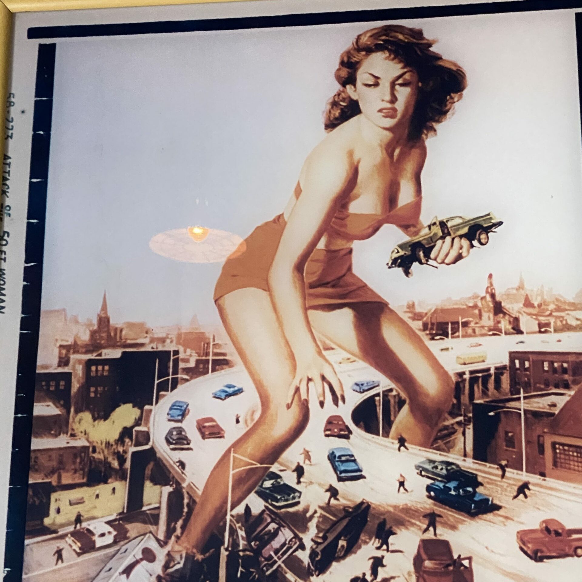 A giant woman holds a car, towering over a chaotic highway with tiny cars and people, set against a cityscape. "Attack of the 50 Ft Woman."