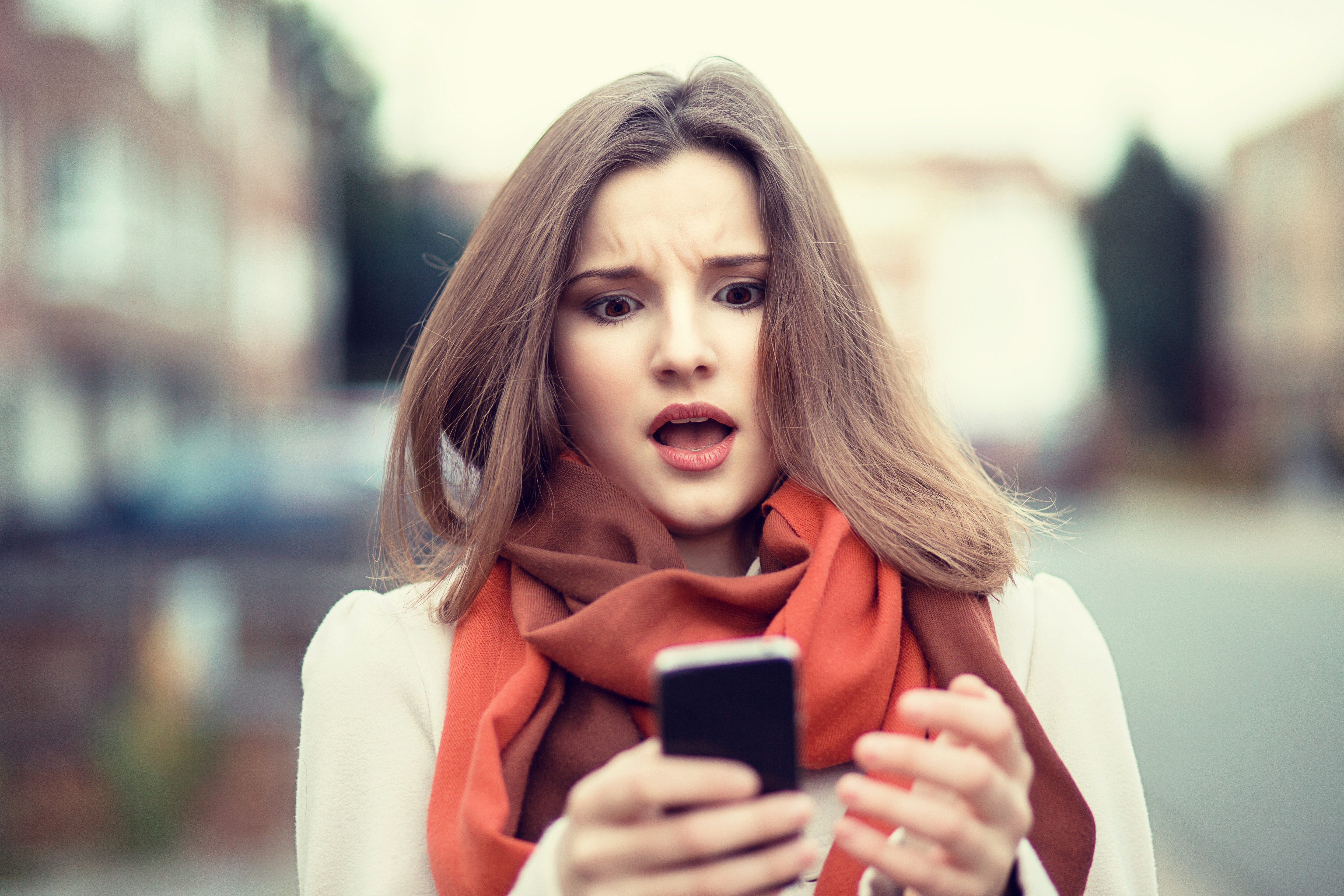 SMS. Closeup portrait funny shocked anxious scared young girl looking at phone seeing bad news photos message with disgusting emotion on face isolated cityscape background. Human reaction, expression