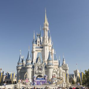 Castle stands tall, show happening on stage, surrounded by trees and a clear blue sky.