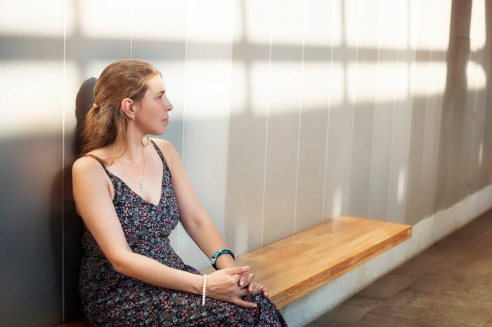 a long-haired brunette in a dress with bare shoulders sits on a bench at the metro station on a hot summer evening and waits for the train