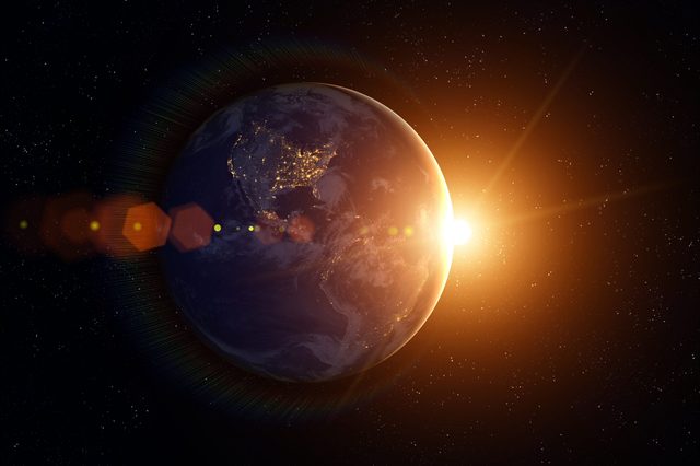 Earth partially illuminated, city lights visible, sun rising; surrounded by stars in space.