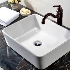 A white rectangular sink sits on a marble countertop, surrounded by a bronze faucet, bar of soap, and small flower vase.