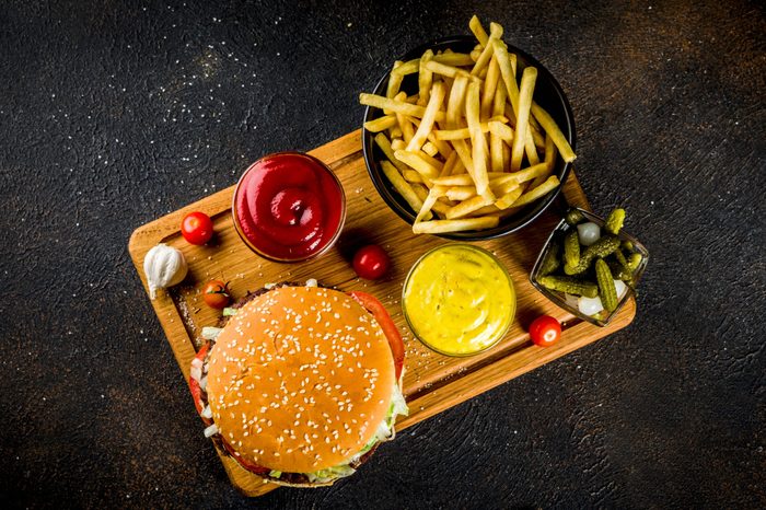 Various party food, Hamburgers, French fries, potato chips, pickled cucumbers, onions, tomatoes and cold beer bottles, rusty black concrete background copy space