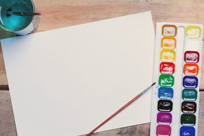 palette of watercolor paints, glass of water and a piece of blank paper on the table.toned.top view