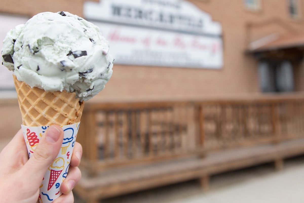Ice cream cone held in hand, outdoors with a blurred, rustic wooden deck in the background.