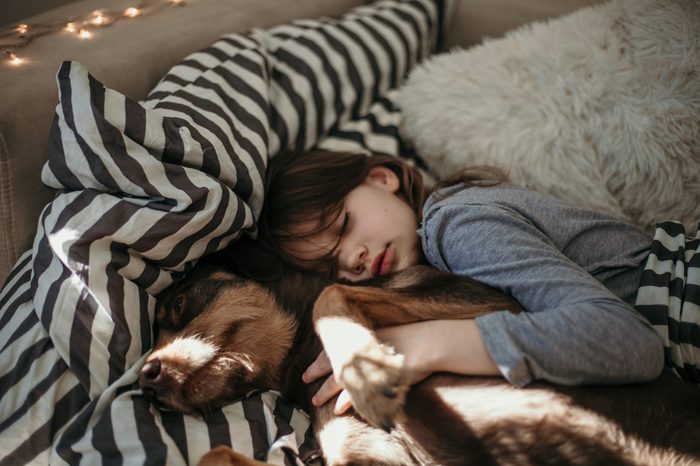Beautiful girl sleeping with her puppy dog. Cuddling and hugging in the bed