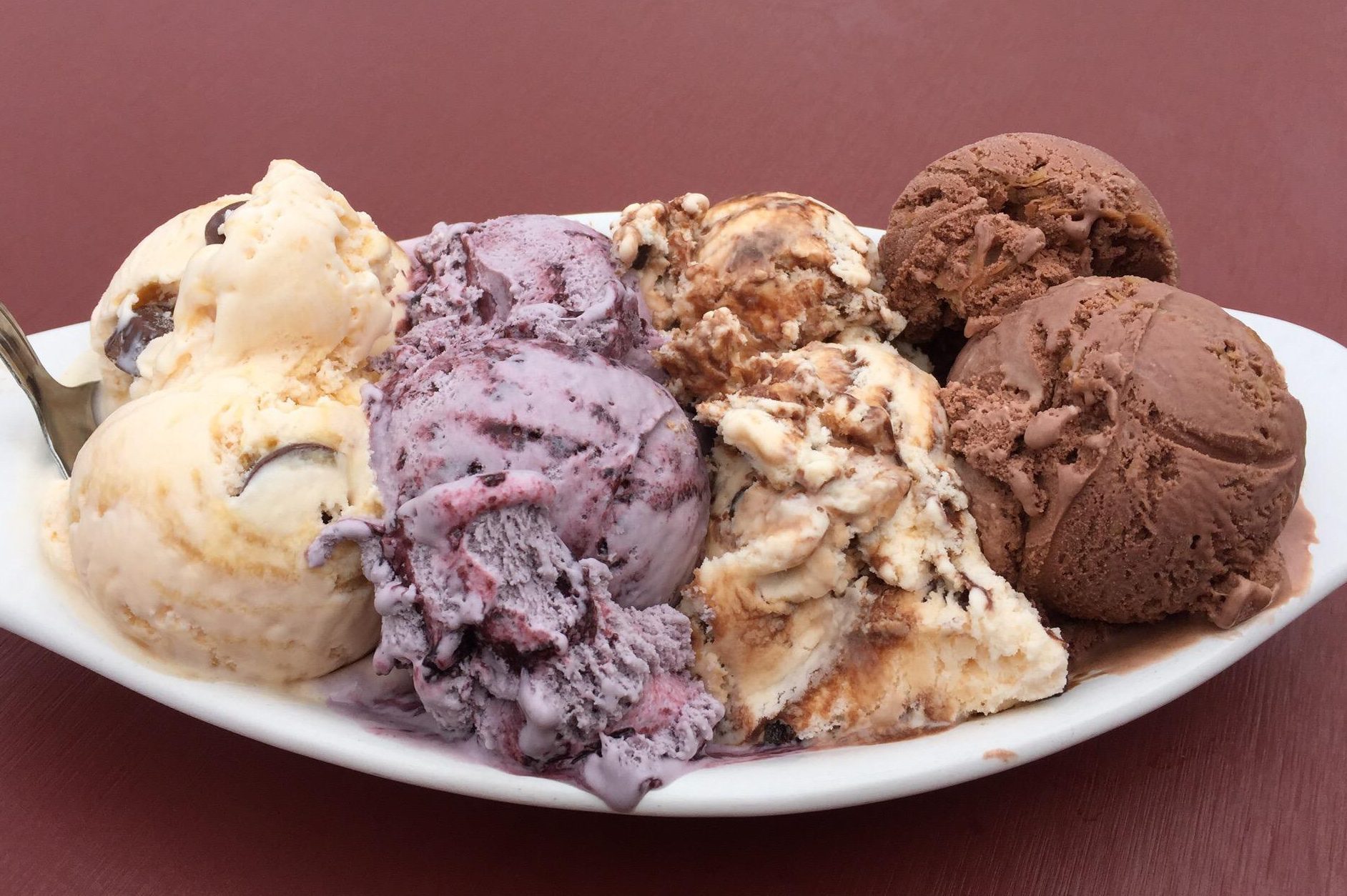 A variety of ice cream scoops rest on a white dish, sitting on a maroon table.