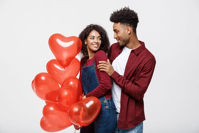 Close up attractive African American couple huging and holding red heart balloon.