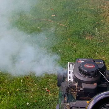 Lawn mower emitting smoke on a grassy lawn.