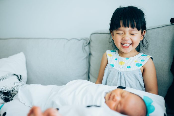 Little sister hugging her newborn brother. Toddler kid meeting new sibling. Cute girl and new born baby boy relax in a sofa. Family with children at home. Love, trust and tenderness