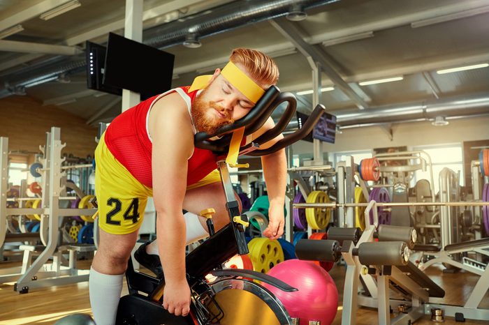 A fat man is tired on a simulator in the gym