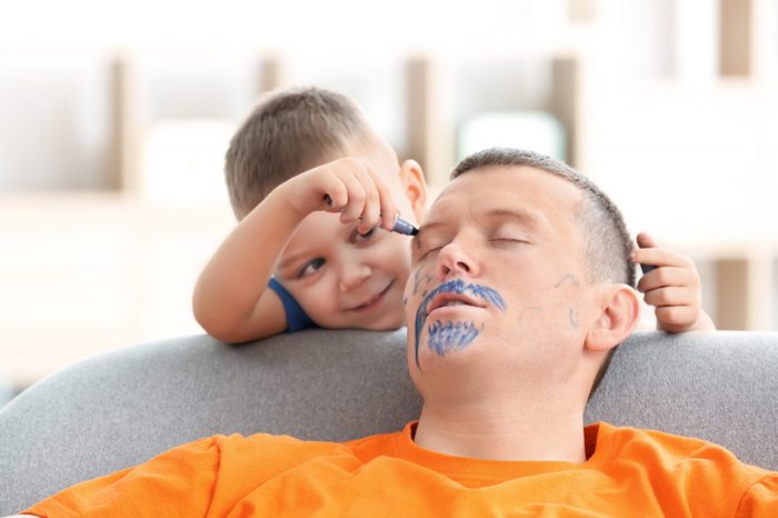 Little boy painting his father's face while he sleeping. April fool's day prank