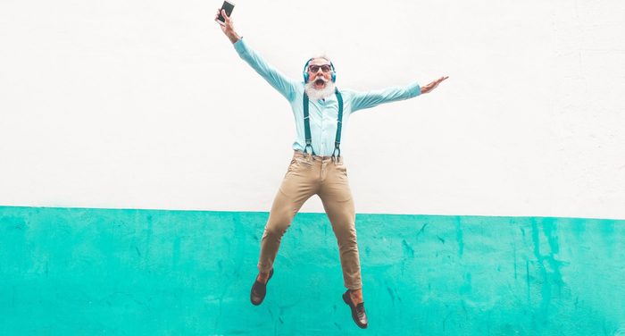 Senior crazy man jumping and listening music outdoor - Happy mature male celebrating and dancing outside - Joyful elderly lifestyle concept - Focus on him
