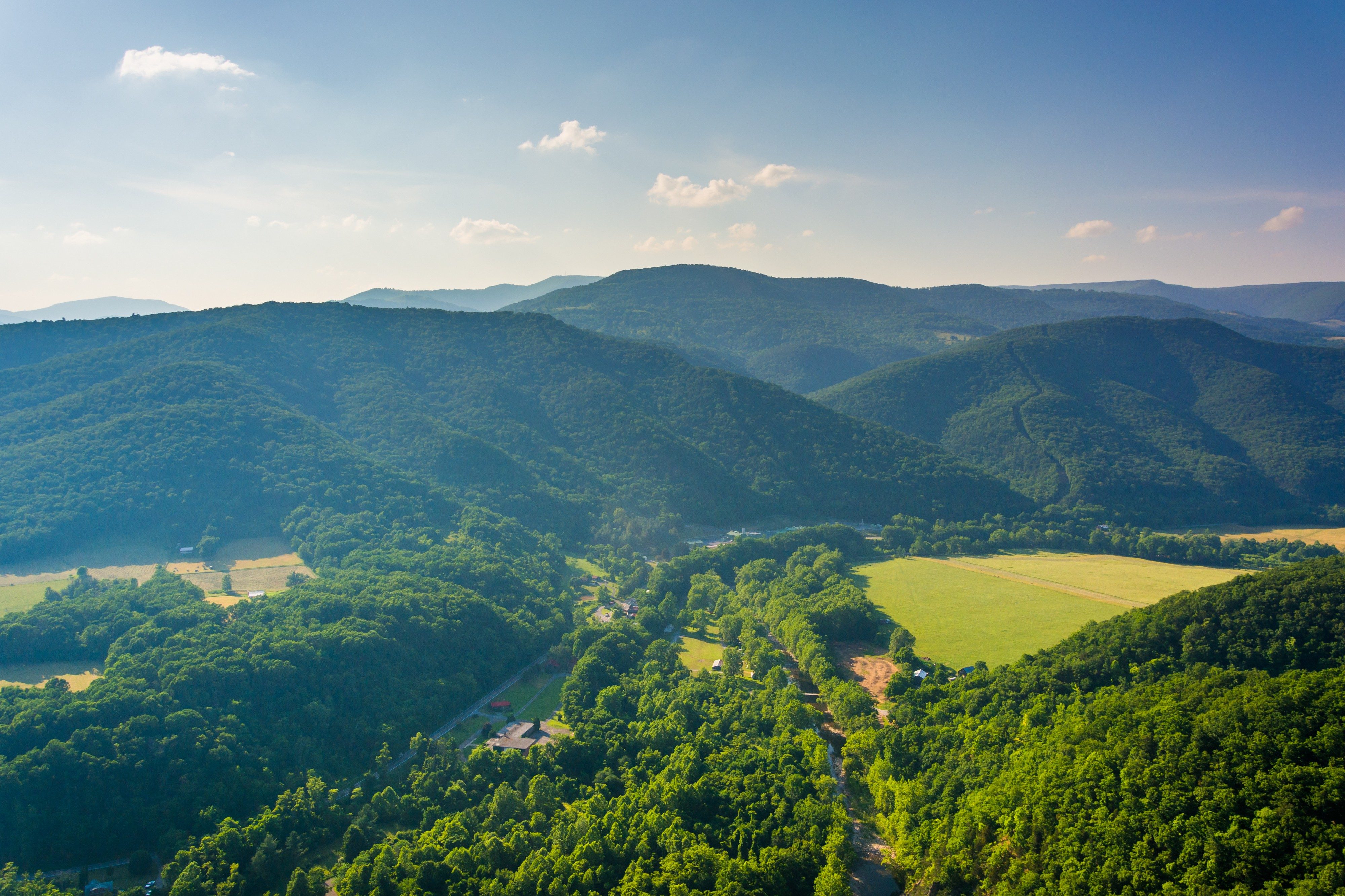 Lush green mountains overlook a scenic valley with fields and scattered buildings under a clear blue sky.