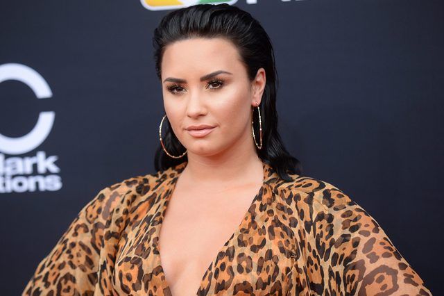 Person posing confidently, wearing hoop earrings and a leopard-print outfit, stands against a black backdrop with partially visible text.