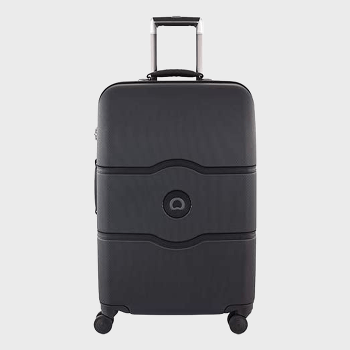 Black suitcase stands upright with an extended handle, featuring four wheels, in a plain, light-colored background.