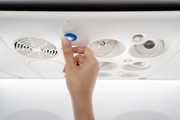 Close up of asian flight attendant's hand call cabin crew or stewardess by pressing help needed button on overhead compartment. Economy class on low cost airline business seated activity concept.