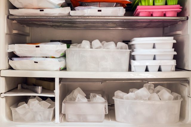 Ice cubes sit in trays and containers, surrounded by various frozen food packages in a refrigerator freezer compartment.