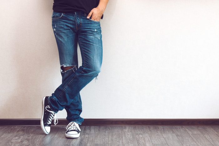 Young fashion man's legs in jeans and sneakers on wooden floor