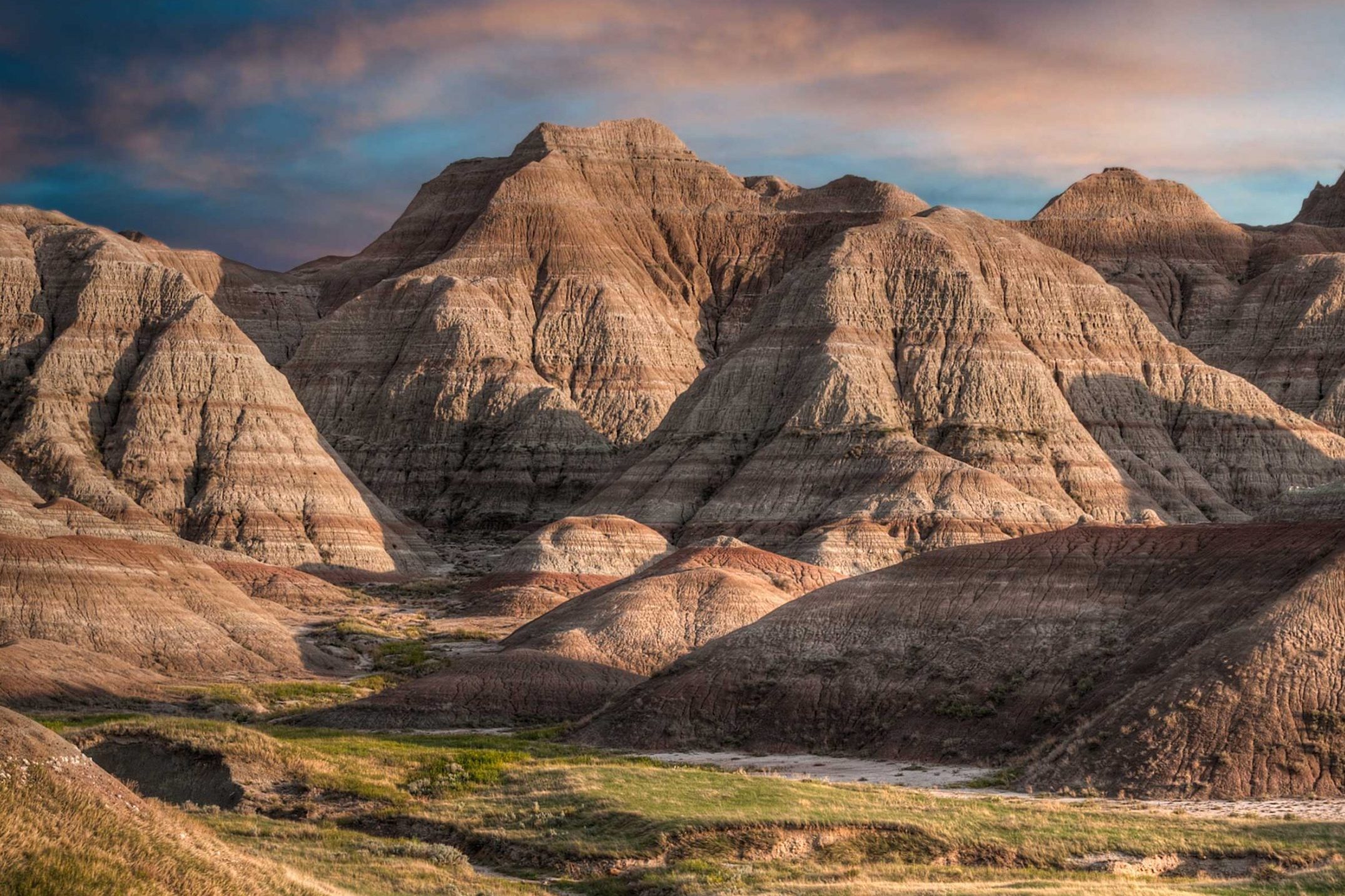 Jagged rock formations rise, towering above grassy plains, under a soft, colorful sky at dawn or dusk.