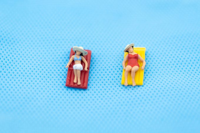 miniature woman wearing swimsuit relaxing on the beach at the sea. Image use for travel business concept. lie vs lay