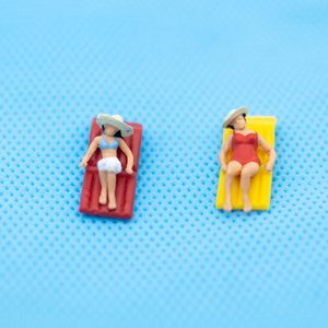 Miniature figures sunbathe on red and yellow loungers against a textured blue background.