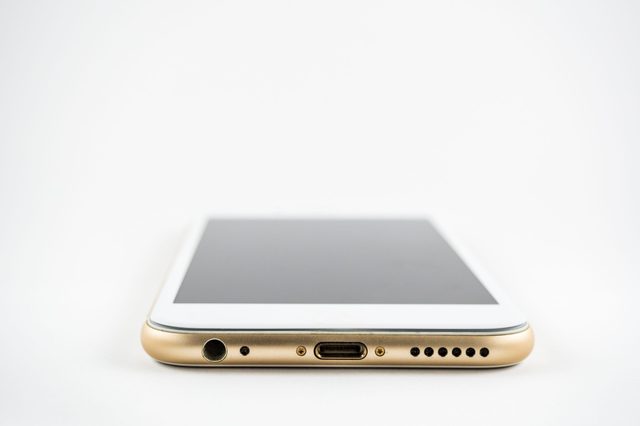 Smartphone lying flat, displaying bottom edge with headphone jack, charging port, and speaker holes, in a minimal white background.