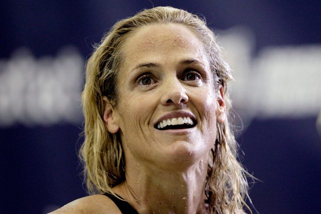 A smiling person with wet hair stands against a blurry, dark blue background.