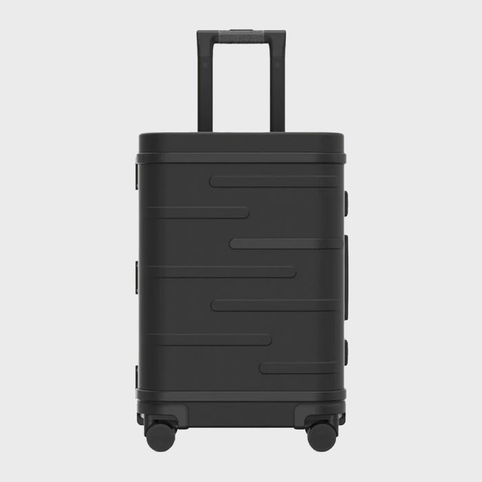A black suitcase, with textured lines, stands upright on four wheels against a plain white background.