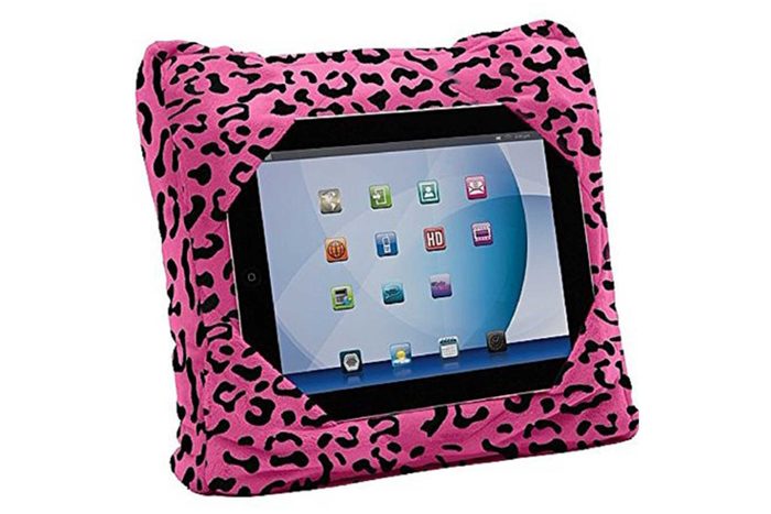 Tablet nestled in a plush pink, black-spotted pillow-like case. The screen displays colorful app icons against a blue background.