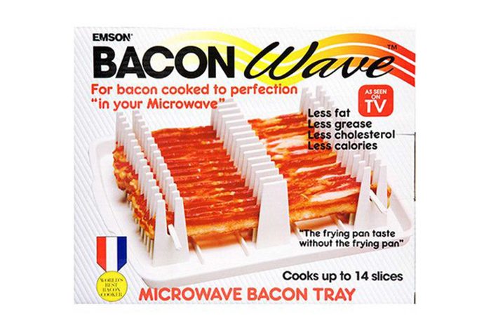 A bacon tray holds bacon slices upright for microwaving, promoting less fat, grease, cholesterol, and calories. Text highlights: â€œCooks up to 14 slices.â€