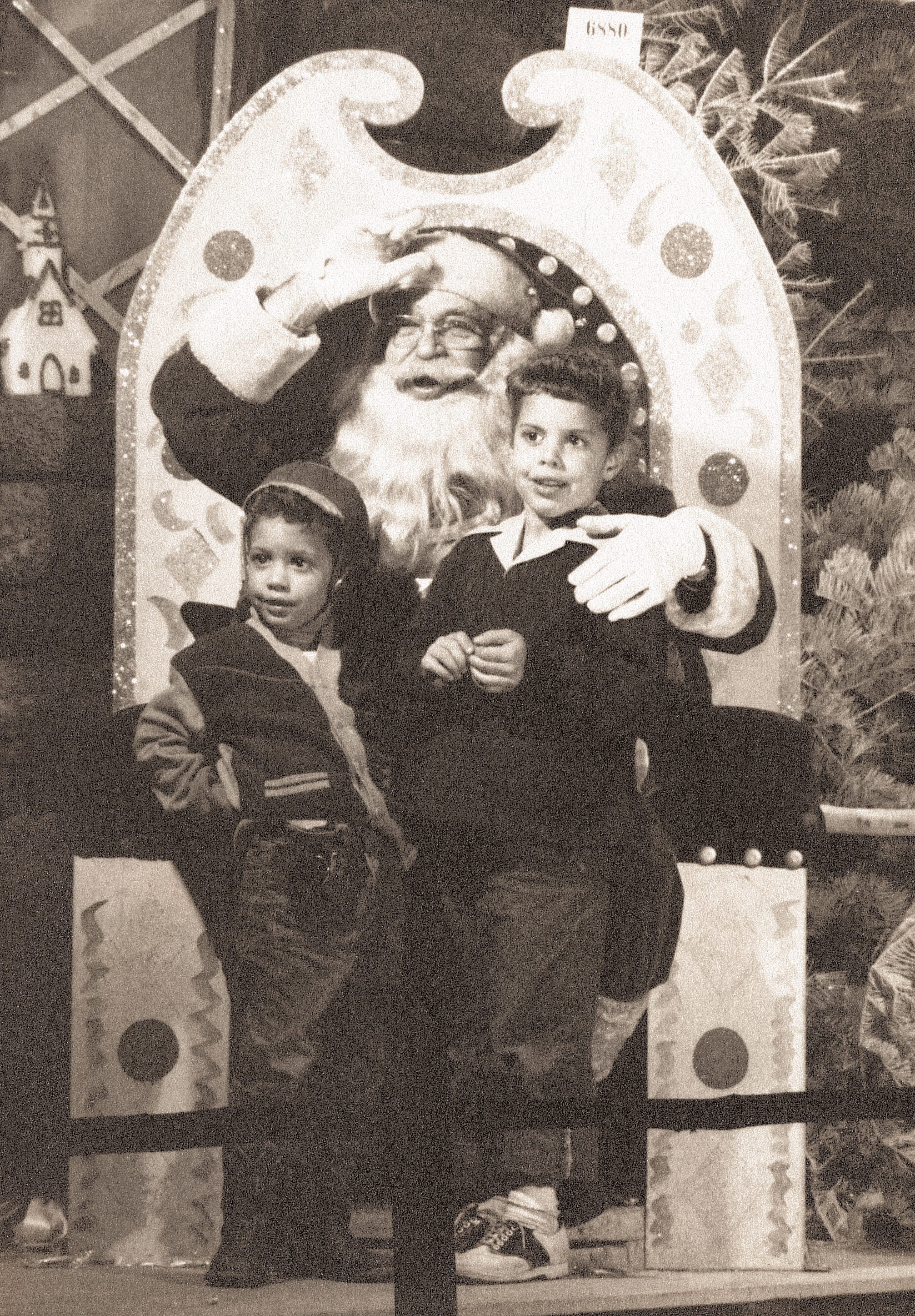 Santa sits on a throne, waving, with two children standing by. The scene is festive, featuring decorative elements and a pine tree.