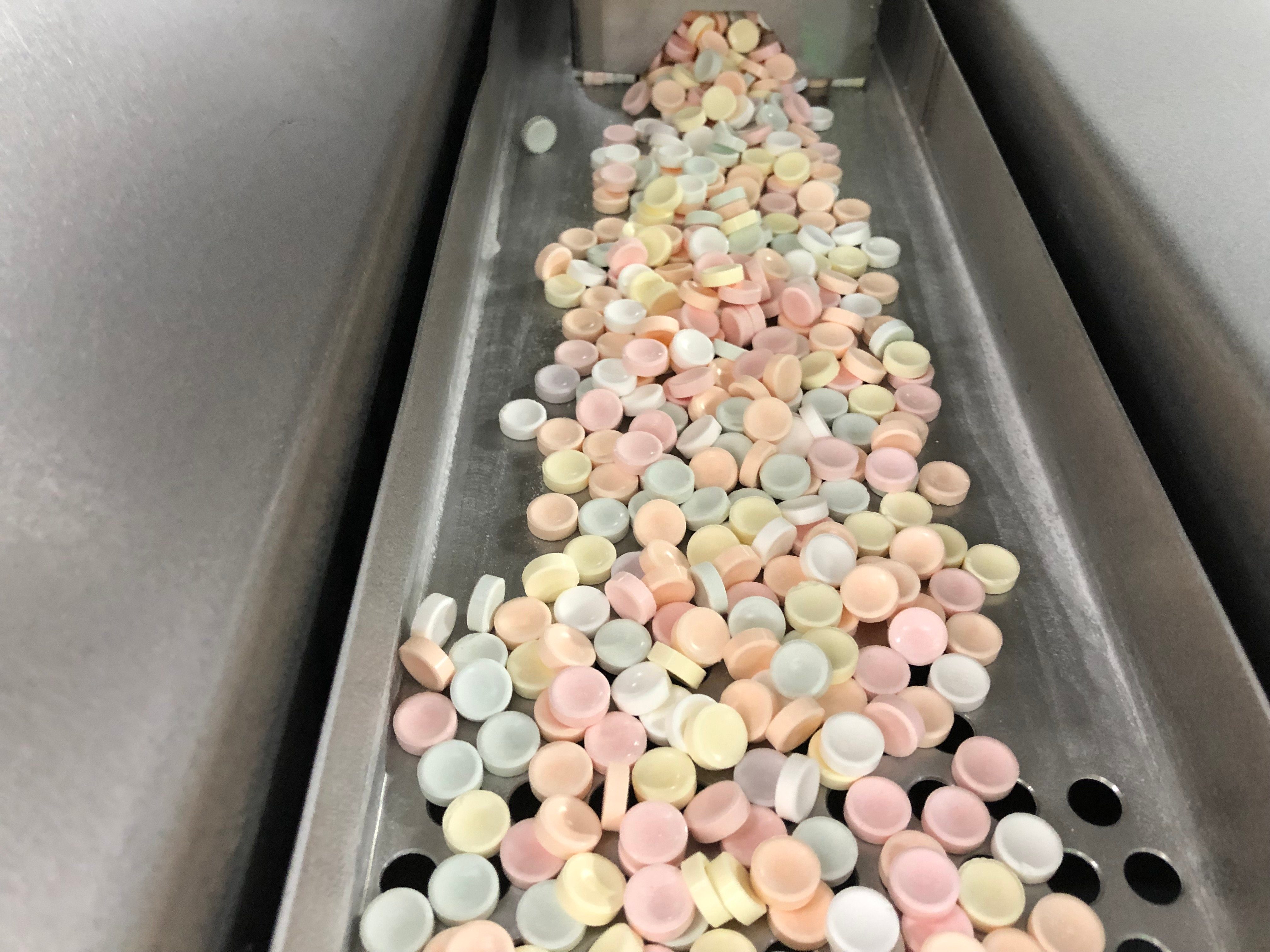 Colorful tablets move along a metal conveyor in an industrial setting.