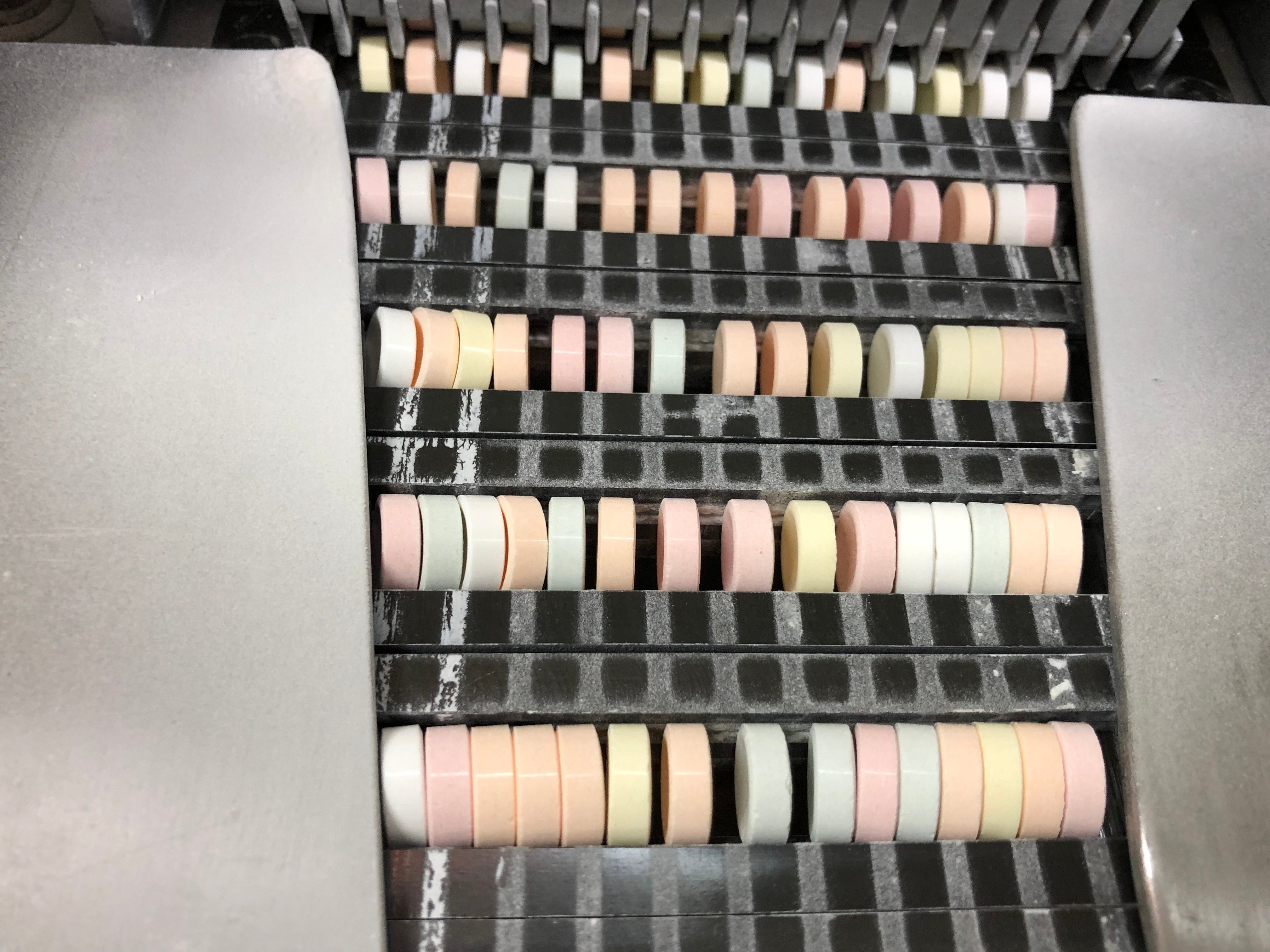Colorful tablets arranged in rows, passing through a sorting machine with metallic components and a textured black surface.