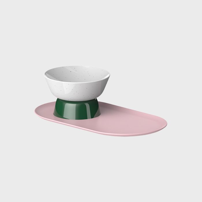 A white bowl rests on a green base atop a pink oval tray, against a light gray background.