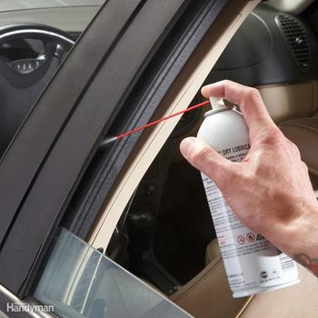 Hand sprays lubricant onto car window seal, inside vehicle, ensuring smooth operation.