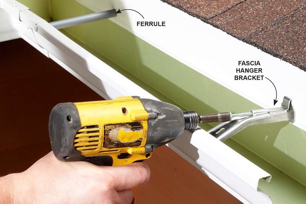 Hand holds power drill attaching gutter to roof, labeled "FERRULE" and "FASCIA HANGER BRACKET," indicating connection points in a home improvement context.
