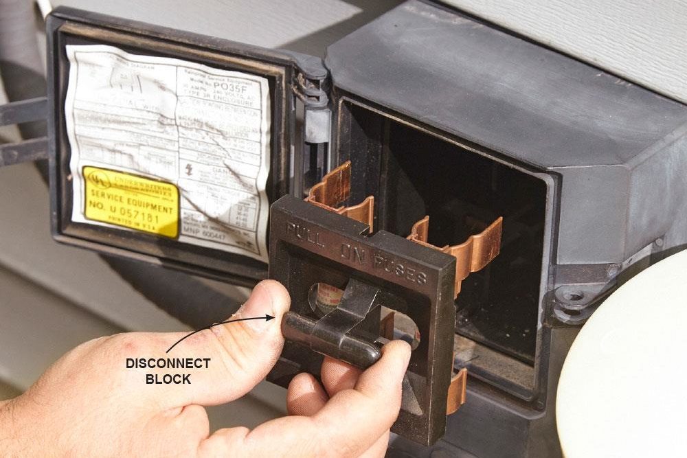 A hand removes a disconnect block from an electrical box, revealing copper connectors. The box has technical specifications inside.